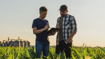 Two men standing in a field looking at a tablet
